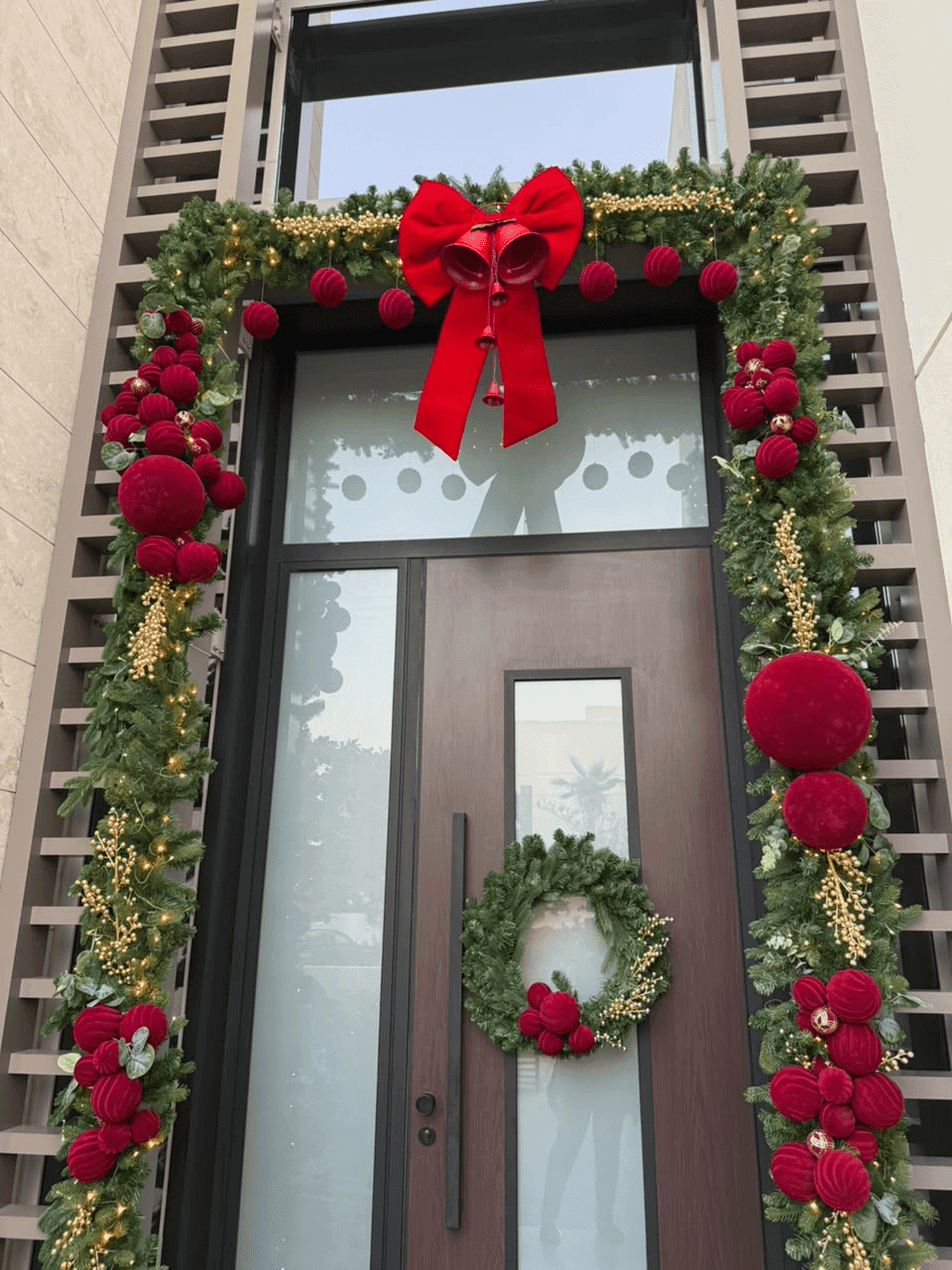 Front door framed with a green garland, red ornaments, a large red bow and a wreath