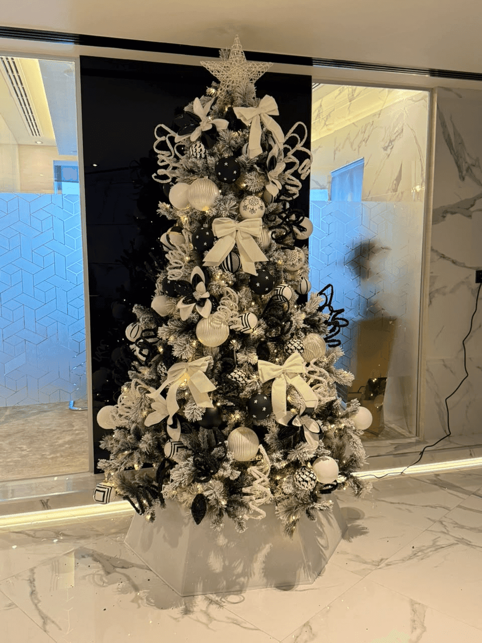 A Pampa Christmas tree styled with white bows, silver ornaments, and a star in a marble interior in Dubai