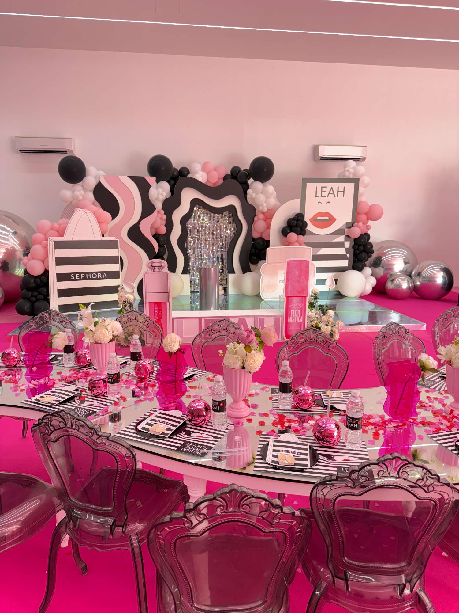 Pink party tables with floral arrangements and a matching birthday backdrop
