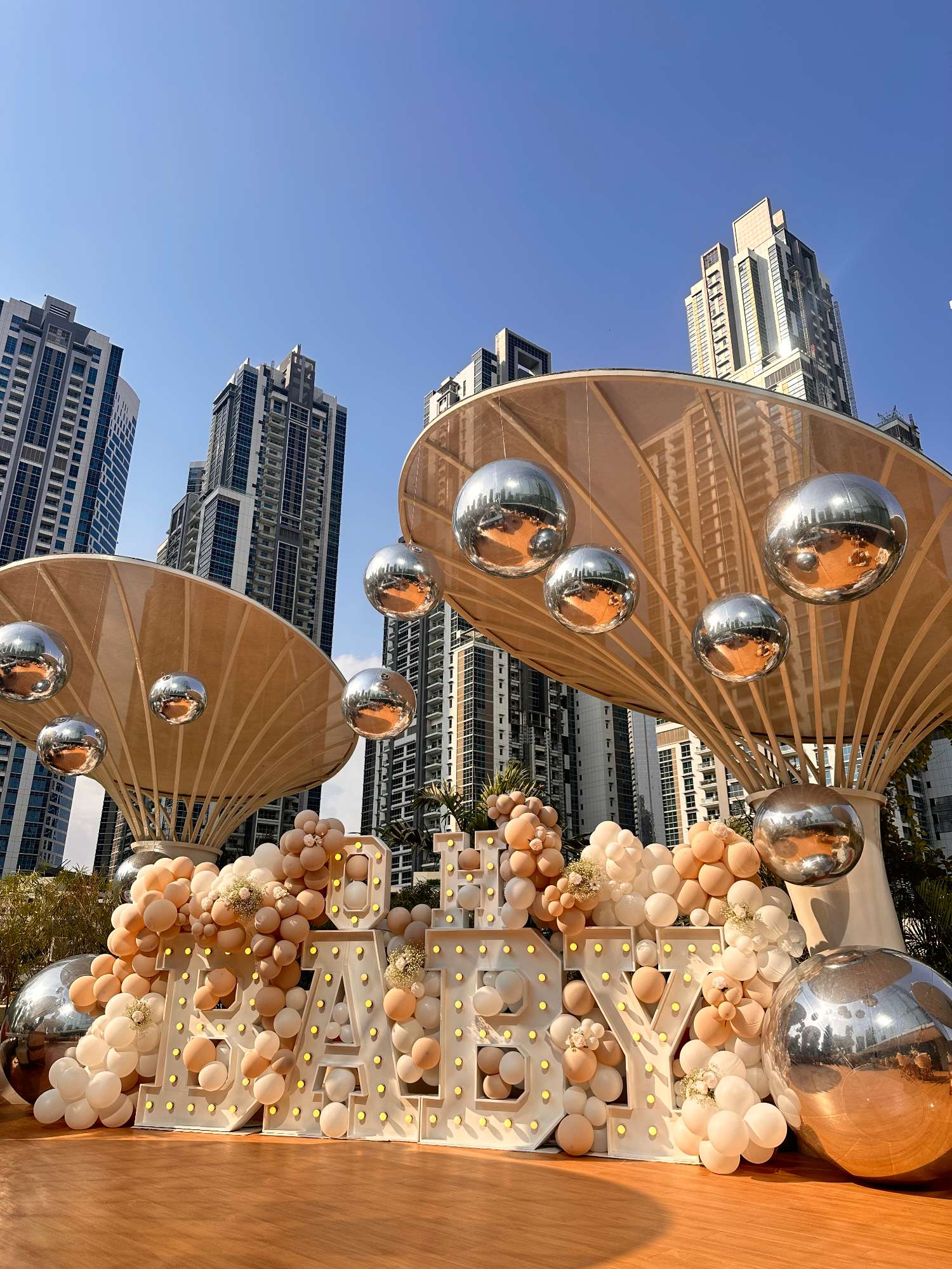 Outdoor milestone setup with illuminated letters, peach balloon décor and reflective hanging ornaments