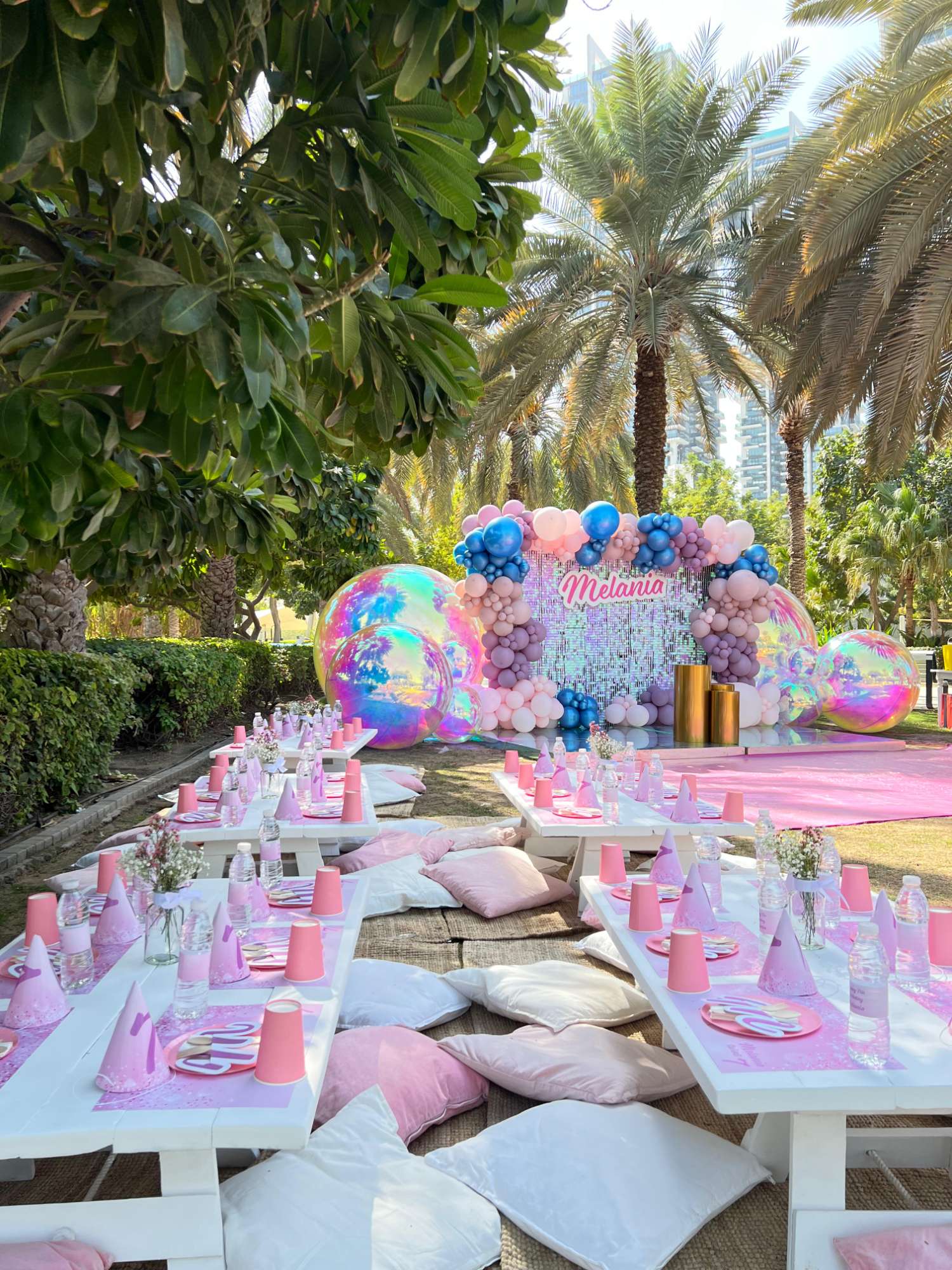 Pink birthday tables and colourful balloons set up in a palm-lined garden