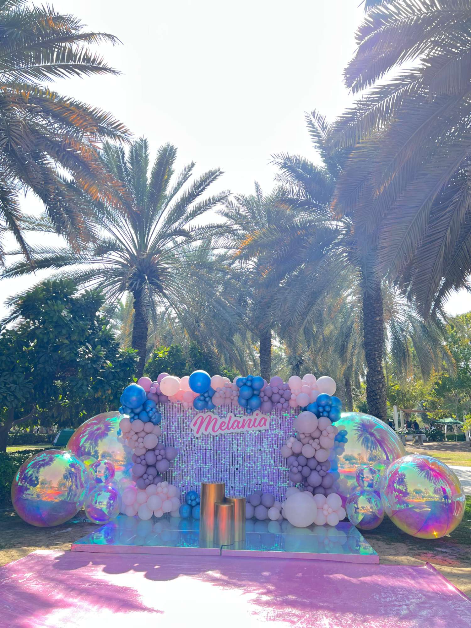 Colourful outdoor birthday backdrop and balloons in a palm-lined garden